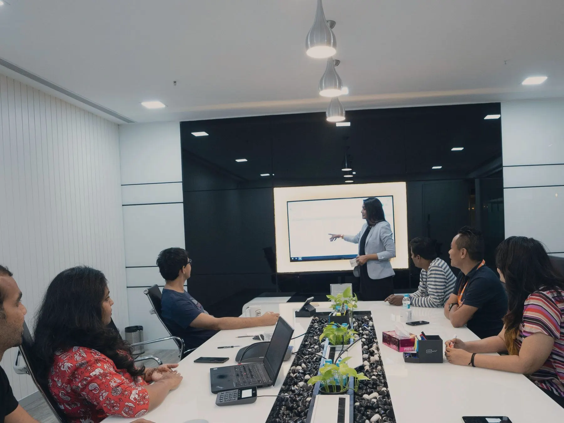 Conference room with a wall-mounted display in use, laptops, table microphones and a desk phone along a long table