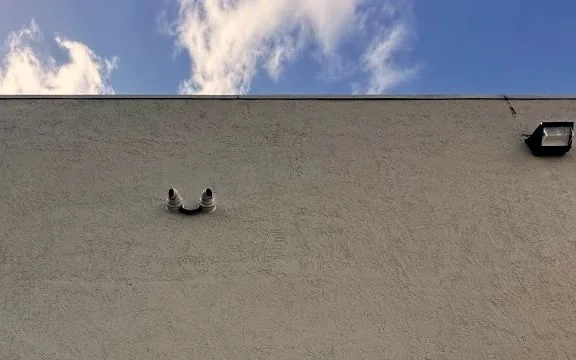 Two dome cameras mounted high on a stucco building elevation just below the roof edge, with a wall-pack light to the right