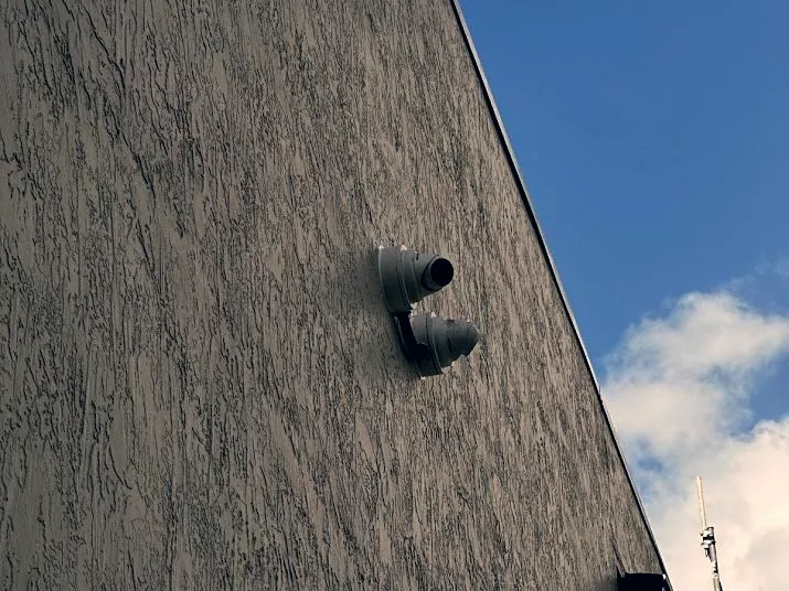 Two exterior bullet cameras mounted on a rendered building wall against open sky