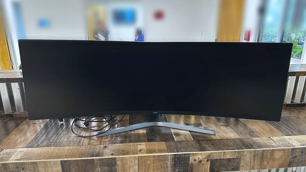 An ultrawide curved monitor set up on a reclaimed-wood reception counter with a corrugated metal front
